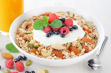 Muesli with fresh berries, nuts and yogurt in a bowl on a light background.
