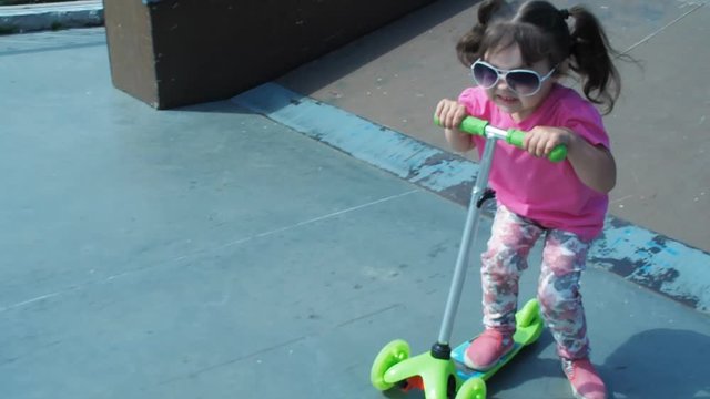 The child is riding a scooter. A little girl is riding a scooter.