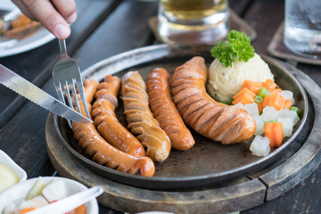 knife cutting German Sausage on hot pan, Mashed Potato and side disk
