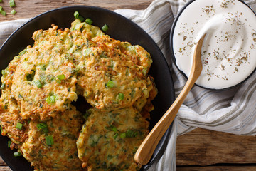 Hot zucchini fritters and sour cream sauce close-up on the table. Horizontal top view