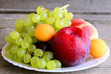 Fresh fruits on a white plate and an old wooden background. Ripe peaches, plums, apricots, grapes branch. Natural healthy food. Summer fruits. Closeup