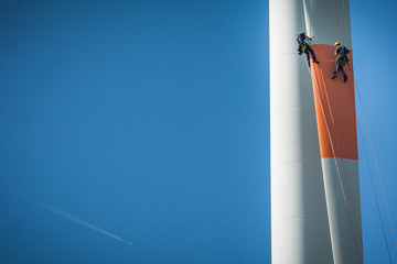 Inspection engineers abseiling down a rotor blade of a wind turbine in a North German wind farm on...