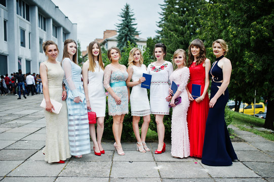 Faulous young women graduates in chic evening gowns posing outside in the park.