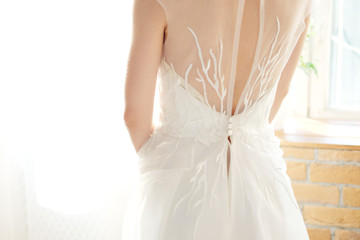 Fototapeta na wymiar Bride in white dress standing near windows view from the back