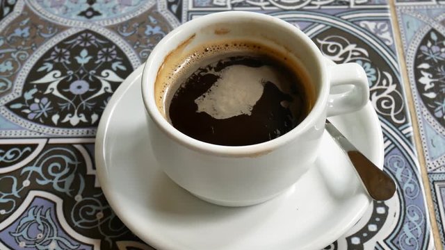 A cup of coffee is a top view. In the mug, the foam from the coffee is spinning.
