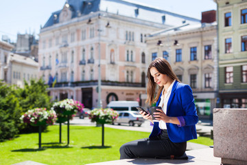 Fototapeta premium Woman checks her phone sitting with cup of coffee on the street