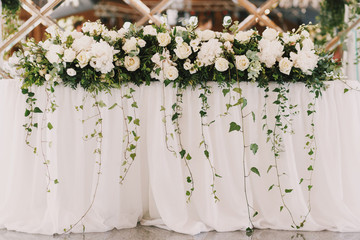 Green branches hang from white rose garland on dinner table