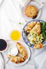 Breakfast in bed. Scrambled eggs with cheese croissants, raspberry muffin and black coffee. Morning treat concept. Horizontal composition with copy space.