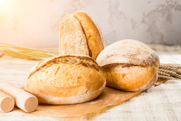still life with a traditional round artisan wheat bread loaves on light background in rays of the sun, shallow dof