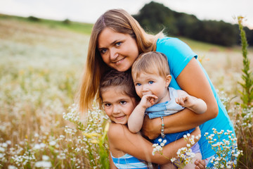 Children hug their mom standing on the field with white flowers