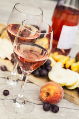Two glasses of rose wine and board with fruits, bread and cheese on wooden table