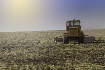 Fototapeta premium Tractor ploughing a field with a trail of dust behind it