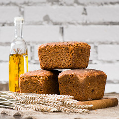 still life with homemade rustic rye breads with seeds, wheat and olive oil bottle on a wooden cutting board, near the wheat. Selective focus