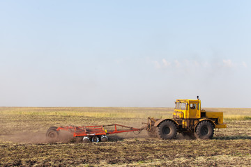 Fototapeta premium Tractor ploughing a field with a trail of dust behind it