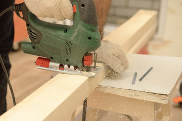 The master saws a wooden beam with a jigsaw