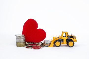 Yellow front loader moving stack of coins with pile of coins and red heart on backgrund, business & financial concept