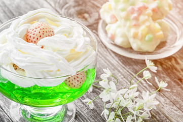 The white dessert of strawberries with cream and green jelly in glass Cup with cookies from marmalade. The small white flowers.