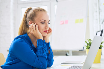 Beautiful young woman sitting at desk looking at laptop on modern home office