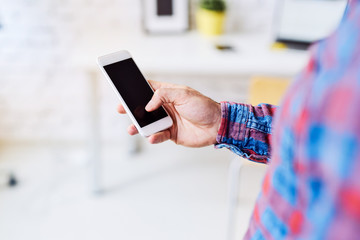 Closeup of young male hand holding phone touching screen in modern office