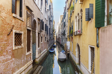 Narrow Venetian canal between colorful houses with boats.
