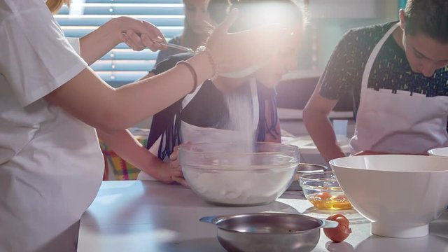 Kids are busy making a dessert at home economics class. One of them is putting flour through a sifter and the others are preparing the dough.