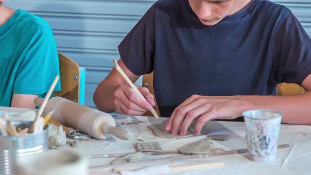 A boy is using different tools to make something from clay in his art class.