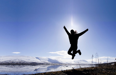 A silhouette happiness woman is jumping with the blue sky background.
