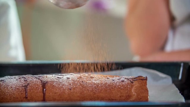 A teacher is slowly sprinking some chocolate on a chocolate cake. Later, she will distribute it to her students.