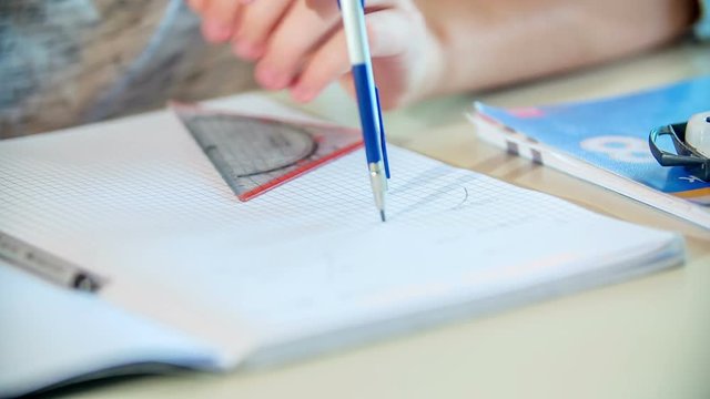 A young girl is drawing a full circle with a pair of compasses into her notebook. They are having a math class.