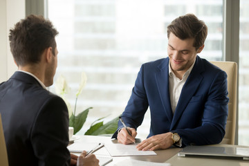 Smiling businessman signing paper at meeting, satisfied entrepreneur concludes contract, holder...
