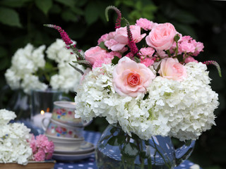 Romantic dinner in the garden by candlelight. Bouquet in a jug of white hydrangeas and pink roses.