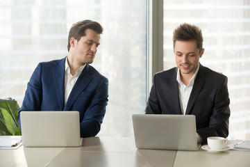 Curious businessman secretly looking at laptop screen of colleague, sneaking peek at other...