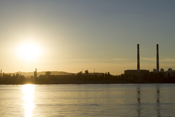 Obraz premium Pipe factory against the background of the river sunset