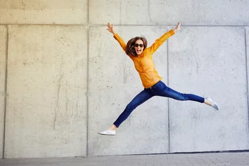 Fotobehang Joyful young lady jumping and raising arms in front of wall outside © baranq
