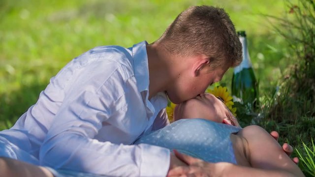 A young couple is kissing on a blanket under a tree and he is also touching her breast. It's summer time.