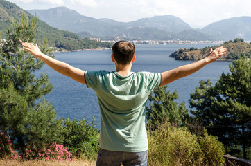 Young beautiful smiling man stretching his arms apart as a bird on a high mountain looking at the sea