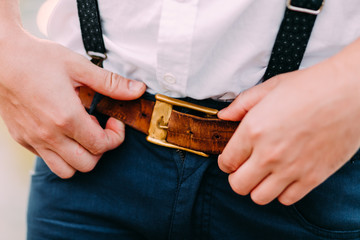 Men's Accessories. Hipster putting on a brown leather belt. Male hands close-up. Clothing concept.