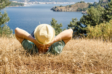 Young beautiful smiling woman in a hat lying on the grass on a high mountain looking at the sea resting and meditating