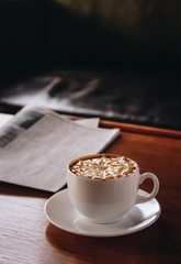 A cup of coffee make latte art by barista with star pattern in a white cup with newspaper on wooden background  in vintage colorใ