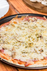 Baked pizza with ham mushrooms grated cheese oregano on the round baking pan on the table