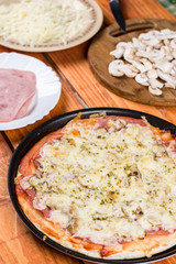 Baked pizza with ham mushrooms grated cheese oregano on the round baking pan on the table