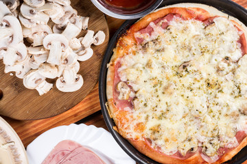 Baked pizza with ham mushrooms grated cheese oregano on the round baking pan on the table