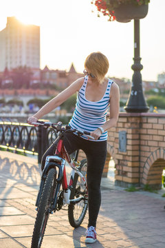 Woman in sunglasses stands with a bicycle on the promenade in the city