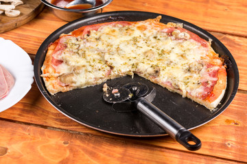 Sliced fresh baked pizza with mushrooms cheese ham ketchup on the round baking pan