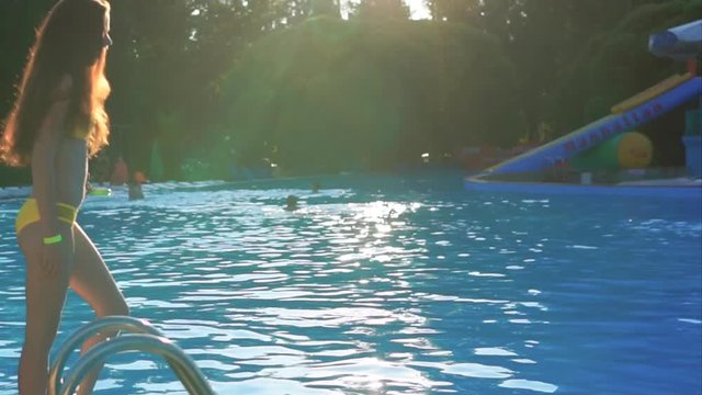 A pretty and young girl who wears a swimsuit jumps into the water in the pool for swimming in the summer, the lady enjoys the summer season and the hot weather