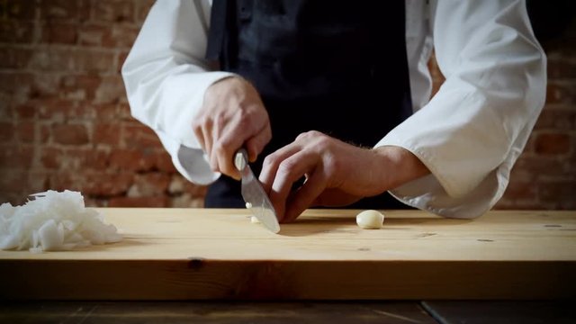 Cookery lessons. The chef cutting two cloves of garlic on wooden chopping board for preparing food. 4K