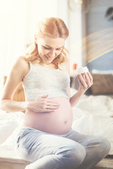 Positive pregnant woman applying boy cream on her belly