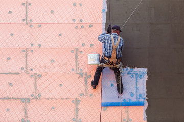 Worker man insulates wall high-rise building