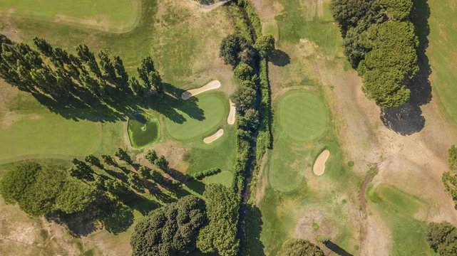 Vista aerea di un campo da golf vuoto con colline verdi e dune di sabbia. Il circolo sportivo &egrave; curato e ricco di alberi e vegetazione.
