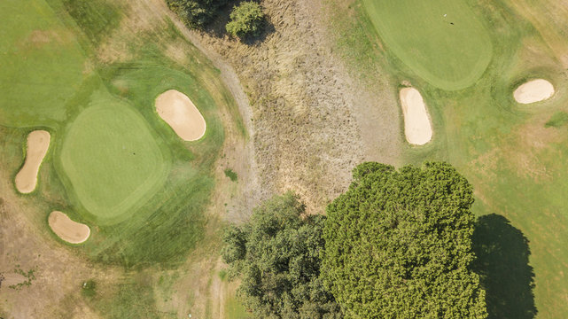 Vista aerea di un campo da golf vuoto con colline verdi e dune di sabbia. Il circolo sportivo è curato e ricco di alberi e vegetazione.